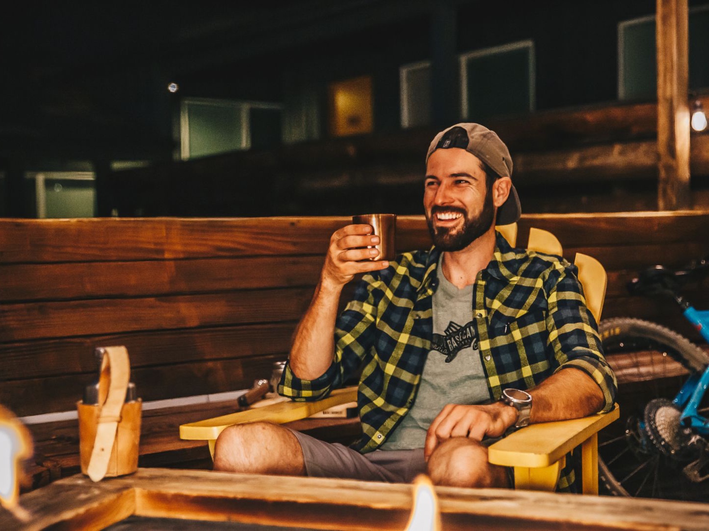 Man sitting around a bonfire while smiling and drinking cocktails with friends.