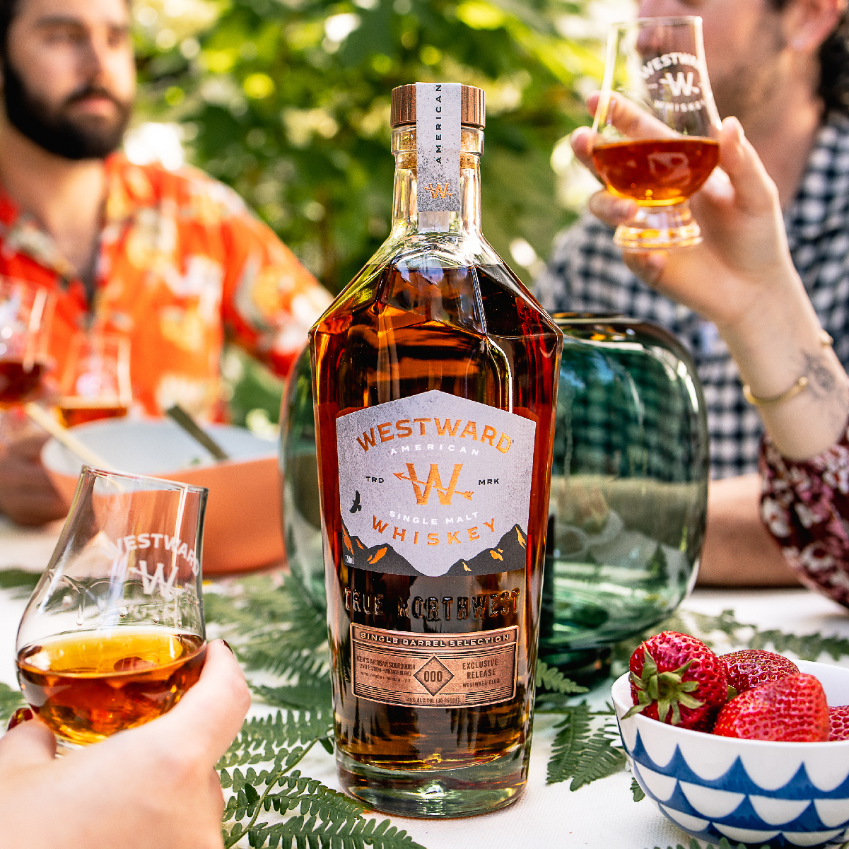 A bottle of Westward Whiskey on a table surrounded by friends.