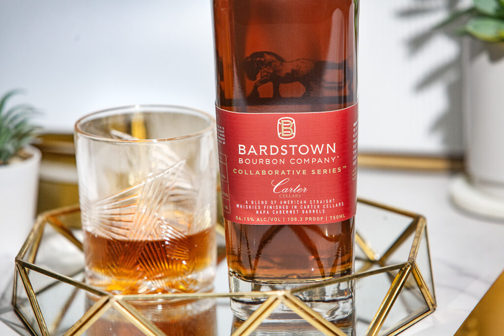 A bottle of bourbon with a low ball glass on a glass table with decor.