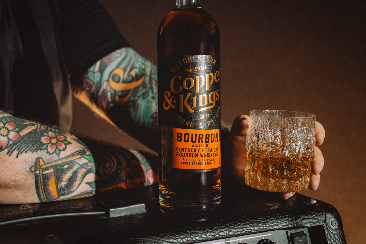 Copper and Kings Bourbon with a glass of whiskey and a man with arm tattoos.