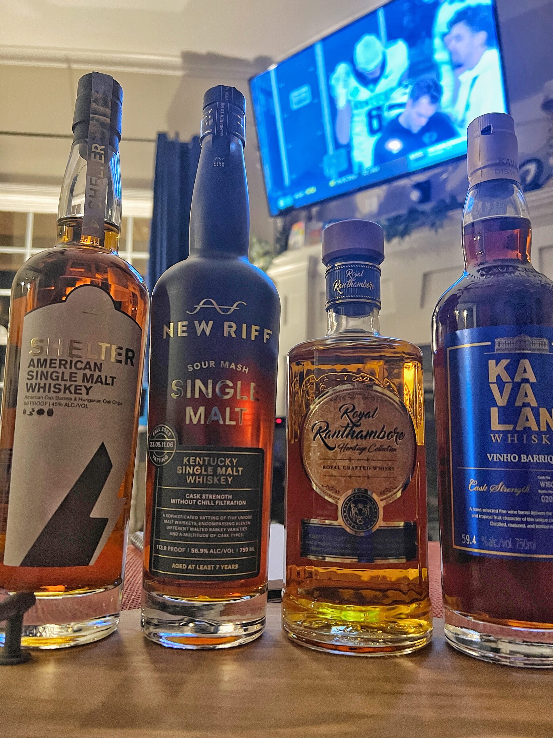 Four Unique Bottles of World Single Malt Whiskeys with a tv in the background