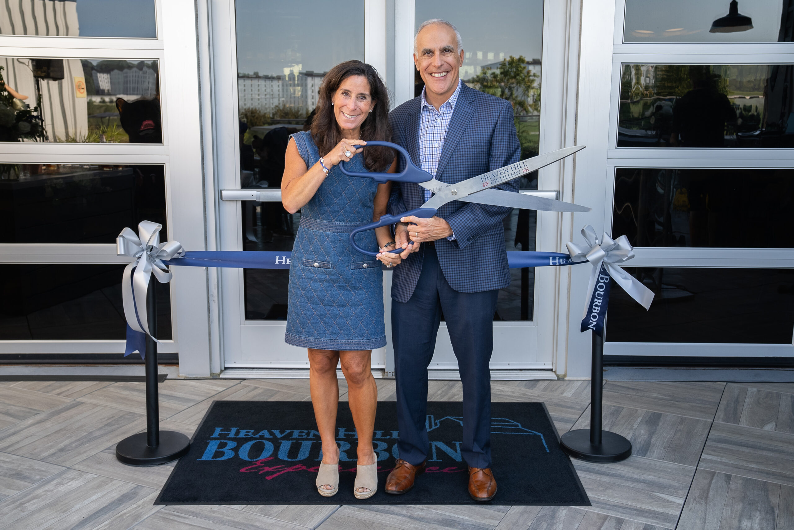 Two people holding giant scissors and the door of a building for a grand opening.