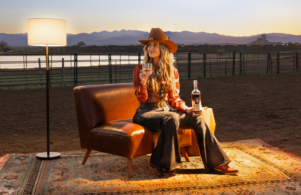 Lainey Wilson on a couch with a bottle of Bourbon