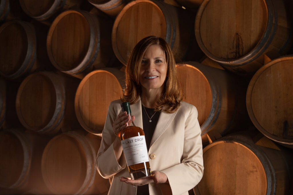 Lady holding a bottle of tequila in front of barrels.