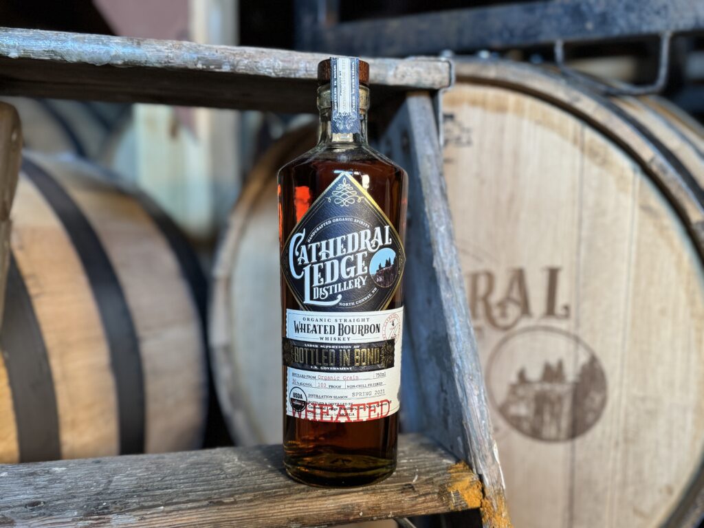 Bottle sitting on a stool with a barrel in the background.