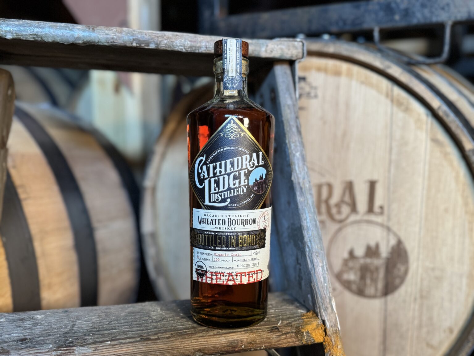 Bottle sitting on a stool with a barrel in the background.