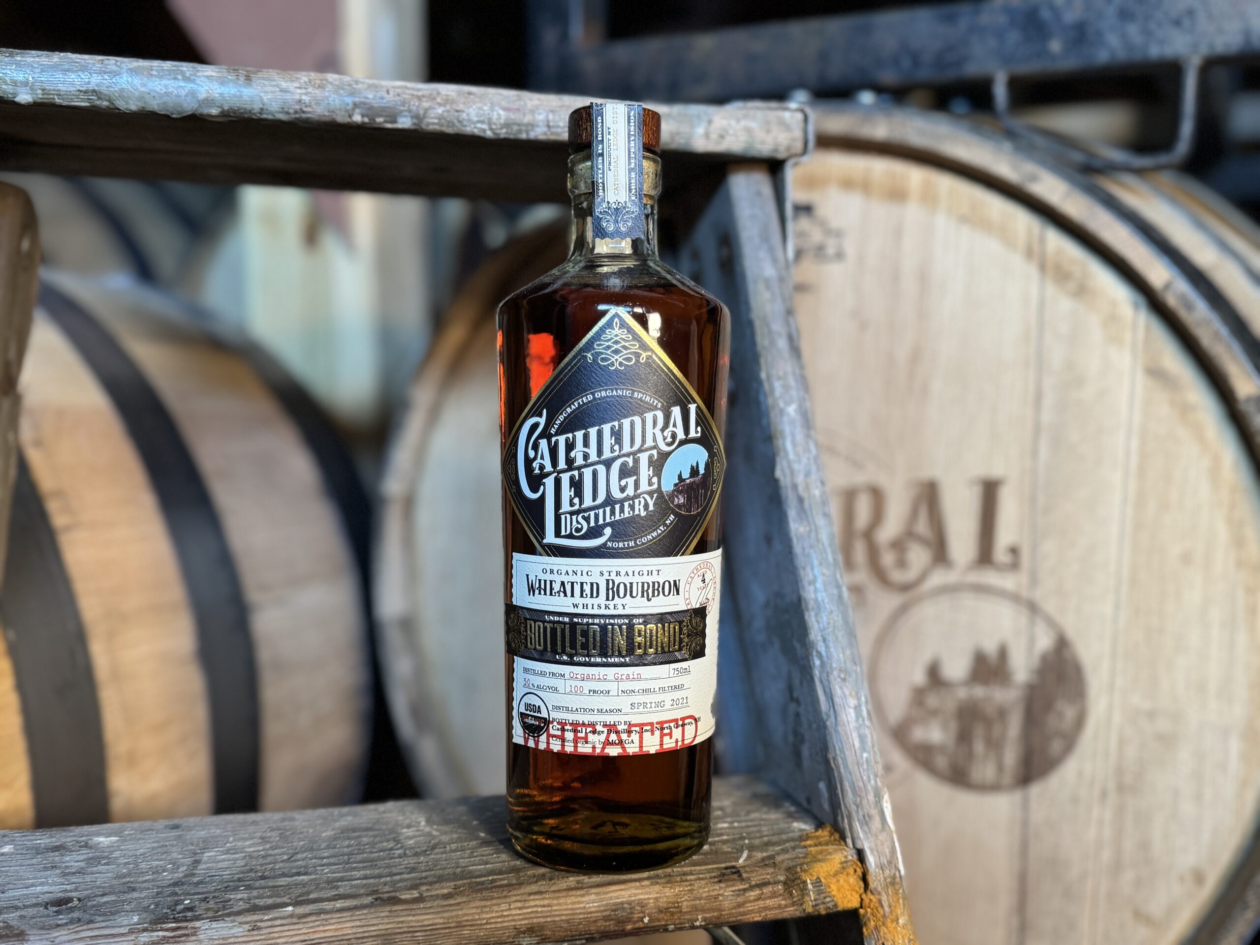 Bottle sitting on a stool with a barrel in the background.
