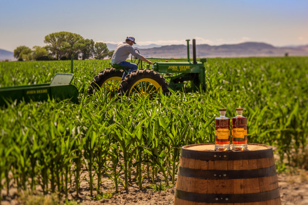 Colby Frey on A tractor in the field with two bottles of Frey Ranch