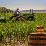 Colby Frey on A tractor in the field with two bottles of Frey Ranch